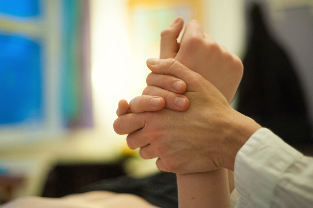 Die Therapeutenhände umfassen ein Handgelenk des Patienten.
